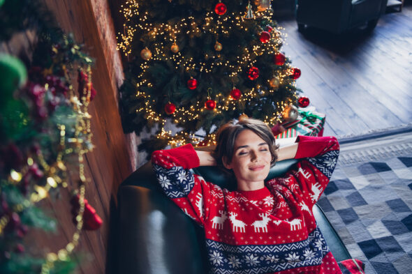 Giovane donna sorridente indossa un maglione di Natale accanto a un albero addobbato