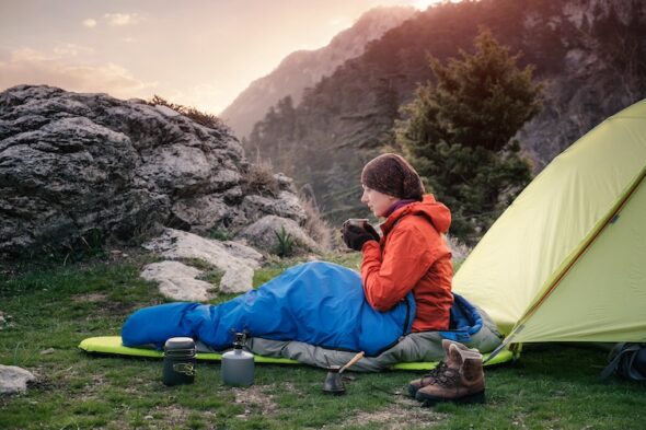 una persona nel sacco a pelo beve il caffè fuori alla tenda